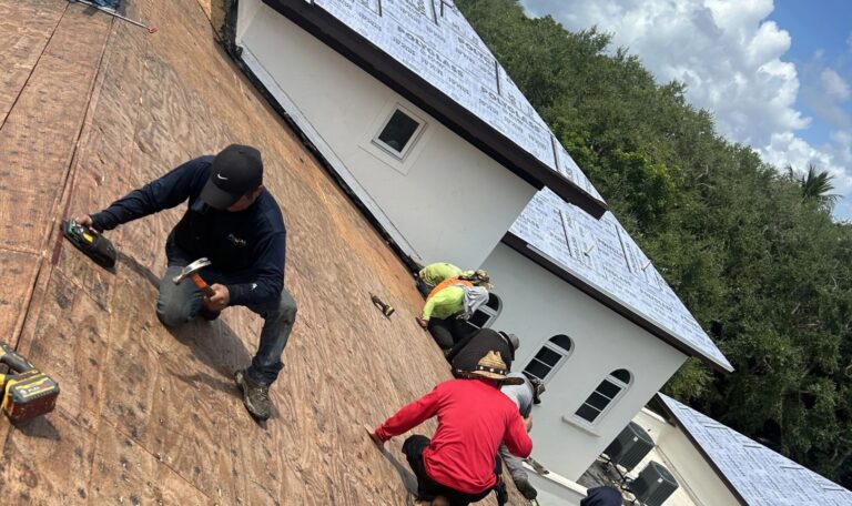 Aerial view of a roofing project in progress with workers laying down roofing materials and managing materials on the ground.