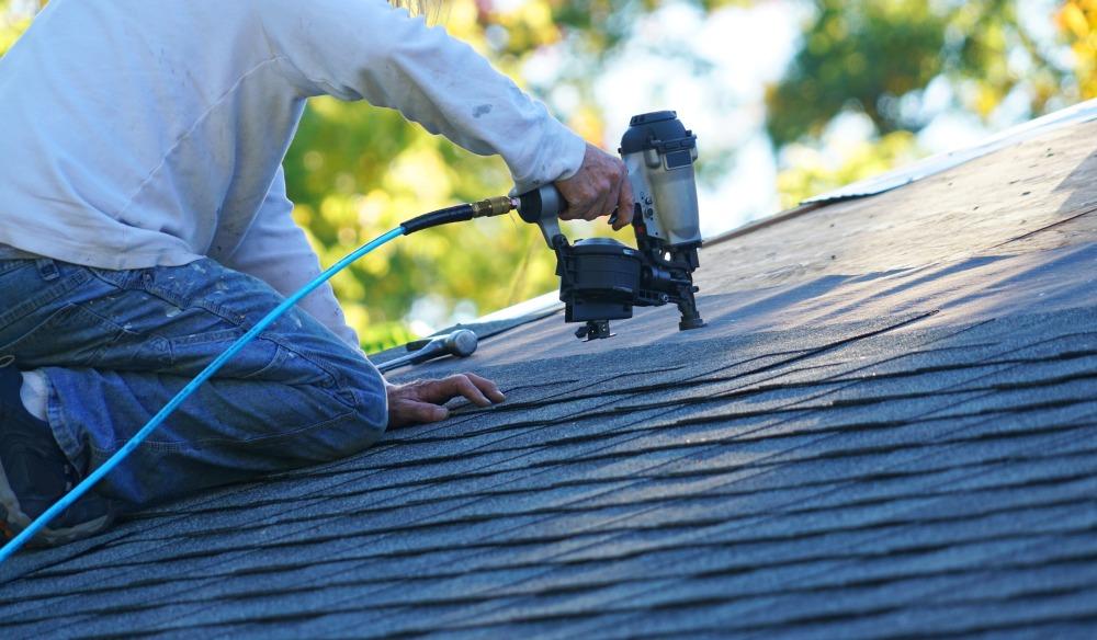 Roofer using nail gun to install shingles