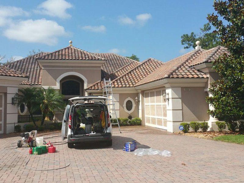 Roofing service vehicle parked in front of a residential home with tile roof, ladder and equipment set up for roof inspection or repair