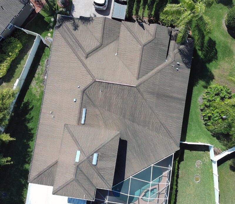 Top down aerial view of a residential home roof with asphalt shingles and screened pool enclosure in a landscaped suburban property