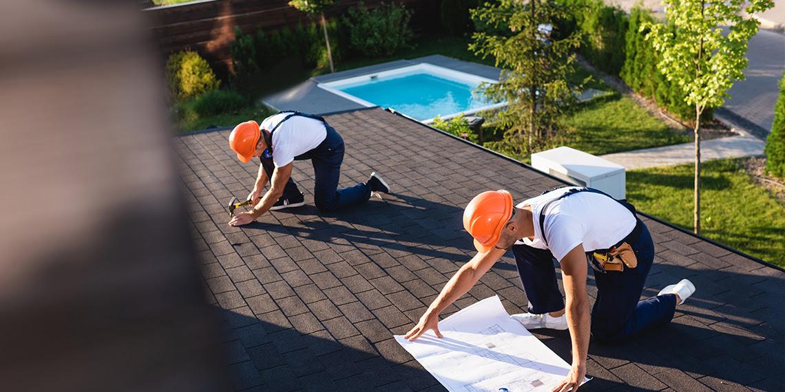 Roofers measuring and installing shingles on residential roof