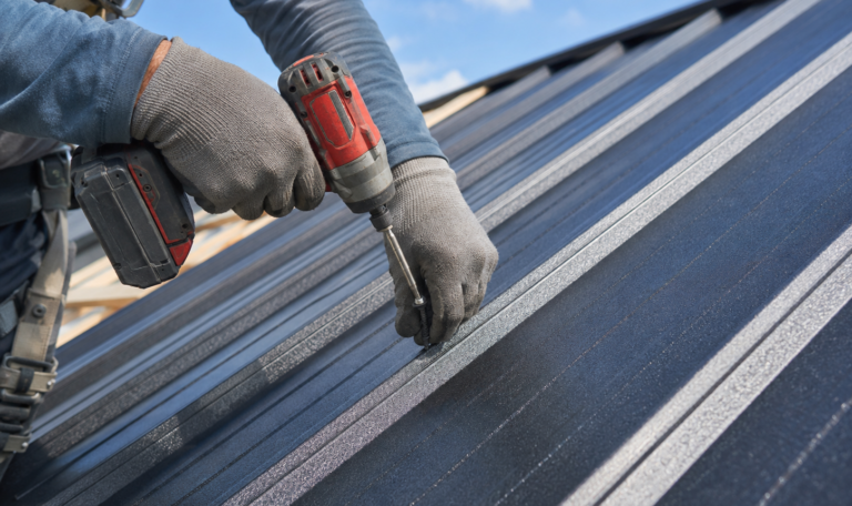 Close-up of a roofer securing a screw into a metal roof panel