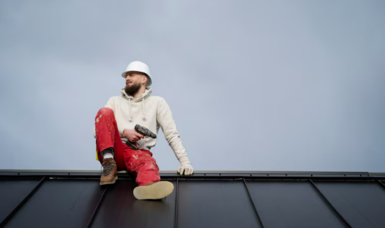 Roofer seated on metal roof holding a drill