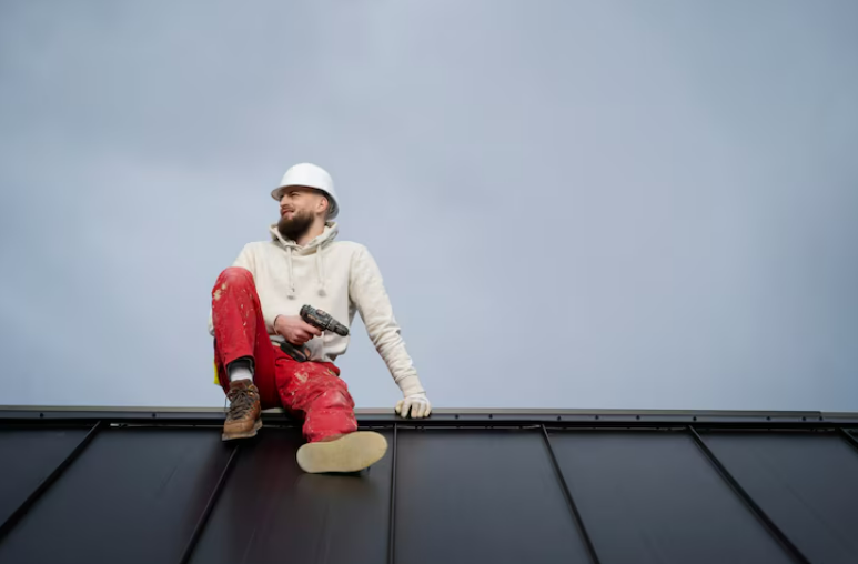 Roofer seated on metal roof holding a drill