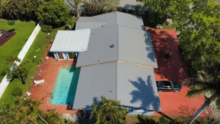 Aerial view of a residential metal roof installation with a backyard swimming pool and paved patio.