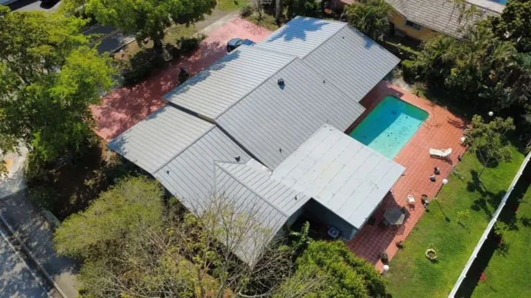Drone view of a gray standing seam metal roof on a residential home with a pool and mature trees.