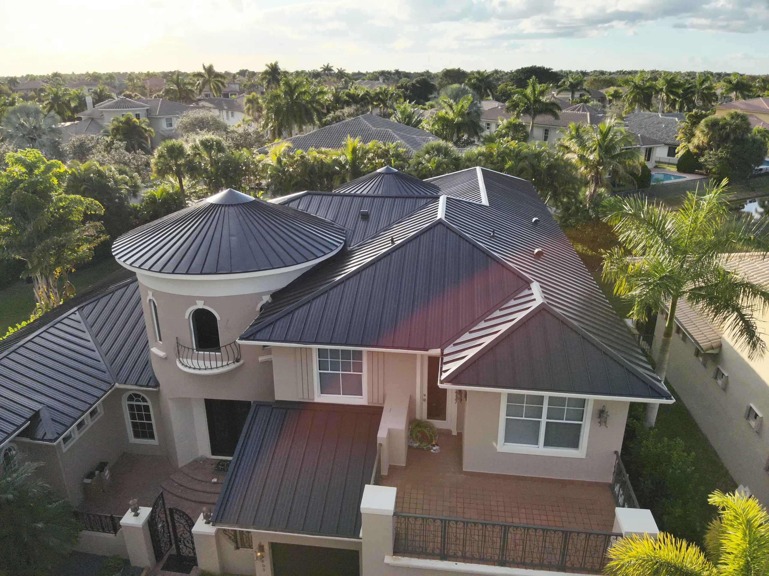 Aerial view of a modern house with dark metal roofing surrounded by palm trees