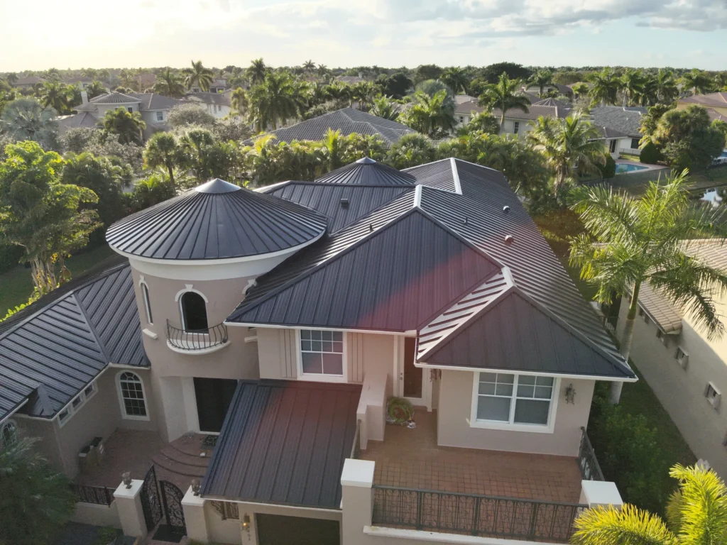Aerial view of a modern house with dark metal roofing surrounded by palm trees
