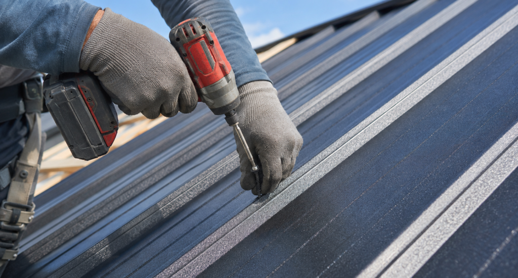 Close-up of a roofer securing a screw into a metal roof panel