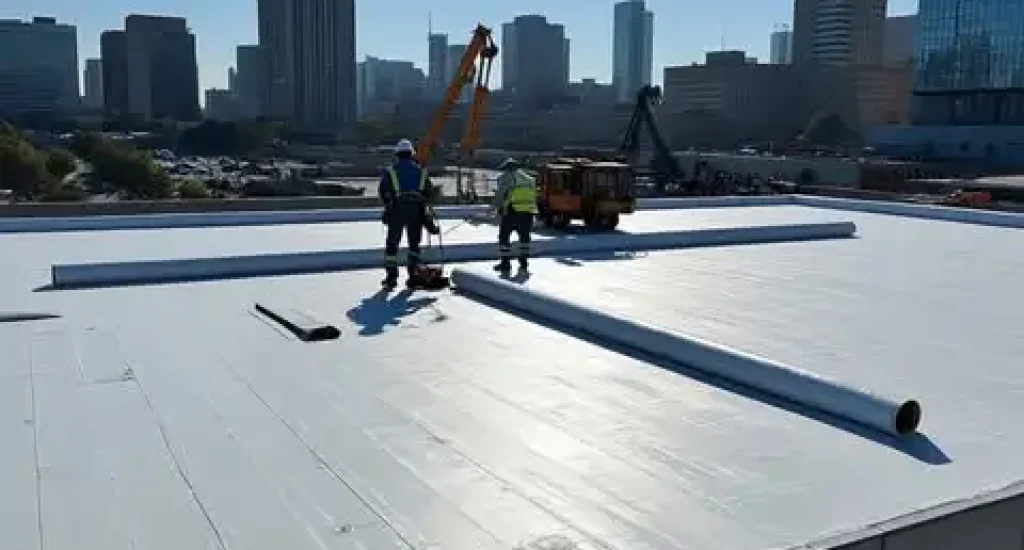 Commercial roofing crew installing a white flat roofing membrane on a modern building.
